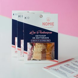 Ketchup bottle with the brand name "Nomie" and the text "Les Fantaisies de Bettina" on the packaging. The ketchup appears to be in a glass bottle with a red cap.