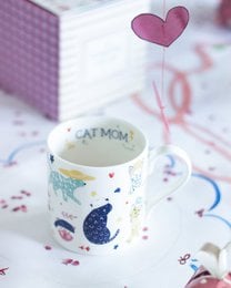 White ceramic mug with "Cat Mom" text, purple cat and heart designs, fine china style.