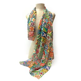 Modernista Tiles Silk Scarf, a vibrant and colorful scarf featuring a patterned design with various shapes and floral motifs. The scarf is made of silk, making it soft and lightweight, perfect for adding a touch of style to any outfit.