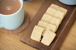 Rectangular light brown biscuits on a wooden board, with a mug of tea in the background. The biscuits appear to be plain and simple in design.