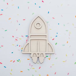 Wooden rocket ship toy with a round window and a small figure. Vibrant colors of orange and red.