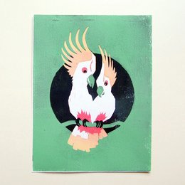 Handprinted woodcut print featuring two vibrant green cockatoos on a green background.