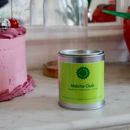  A tall, round, green tin candle with the "Matcha Club" logo. The candle appears to be a scented candle, likely with a matcha or green tea fragrance.