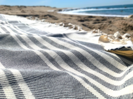 Striped beach towel in white and gray colors, made of soft, absorbent material, suitable for use at the beach or pool.
