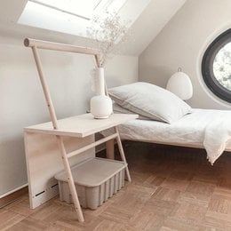 Adjustable wooden table with a minimalist, modern design suitable for a child's bedroom. Features include a light wood finish, a height-adjustable surface, and storage compartments.