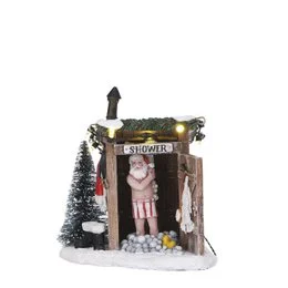 A miniature white plastic Christmas village scene with a small Santa figure, snow, and decorative elements.