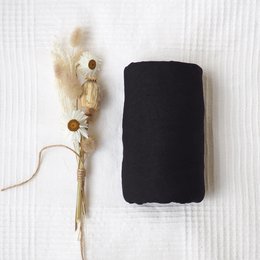 Black swaddle blanket made of soft, breathable fabric. Features tasseled accents for a stylish touch.