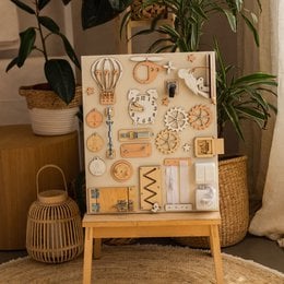 Beige busy board with various sensory elements including shapes, textures, and colors for toddler play and exploration.