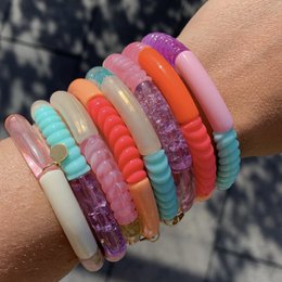 A colorful tube bracelet made of beads in various shades of orange, pink, and turquoise. The bracelet has a textured, twisted design that adds visual interest.