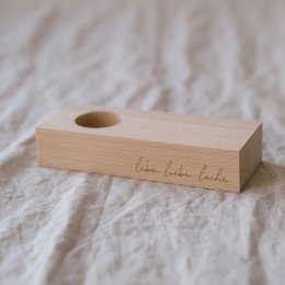 Wooden egg cup with "Live Love Laugh" text, made of light-colored wood, rectangular shape with a circular hole for holding an egg.