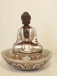 A silver-colored Buddha statue sitting in a meditative pose on an ornate, circular base.