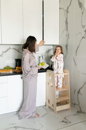  A tall, wooden learning tower with a natural, delicate blue, or pink finish. The tower features a step stool design with multiple levels, allowing children to safely reach higher surfaces. Suitable for use in the kitchen or other areas of the home.