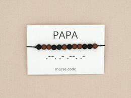 A black and brown beaded bracelet with the word "PAPA" written on a card, representing a Morse code bracelet for a father.