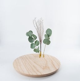 Vase Astrid, made of ash wood, with a round, minimalist design and featuring green eucalyptus leaves and dried floral accents.