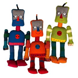 Colorful, whimsical plush robot figures in various shapes and designs, including a tall, round robot with a red body and blue accents, a shorter robot with a green and orange striped body, and a robot with a rectangular body and large eyes.
