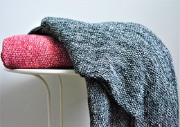 Cozy gray and pink knitted throw blanket, round black and white patterned rug, woven basket with household items.