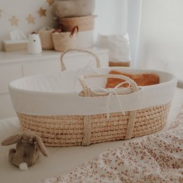 Soft, cozy white Moses basket with woven accents, perfect for a nursery or child's room.