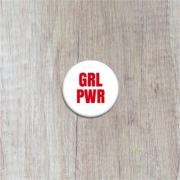 A round, white button with the text "GRL PWR" printed in red. The button appears to be a feminist or empowerment-themed accessory.