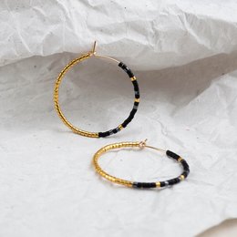 Gold-tone hoop earrings with black beaded accents. Circular shape with a modern, minimalist design. Suitable for casual or formal wear.