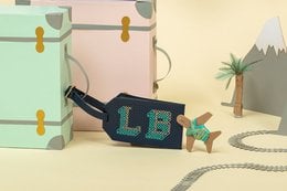 Navy blue luggage tag with the word "LE" embroidered in a stylized font. The tag features a geometric design with triangular shapes and a palm tree icon, suggesting a travel or vacation theme.