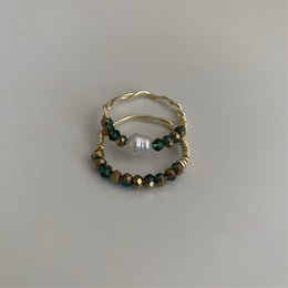 A gold-colored ring with green, gold, and pearl-colored beads. The ring has a twisted, textured band design.