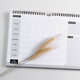 A weekly planner with a spiral binding and a wheat stalk or ear of grain placed on top of the calendar grid.
