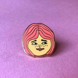 A colorful enamel pin featuring a stylized illustration of a girl's face with vibrant pink and orange hair. The pin is described as a "Girl Enamel Pin" and is categorized as a brooch.