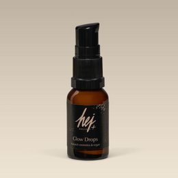  A small brown glass bottle with a black spray nozzle, labeled "Hej+ Glow Drops 14ml". The bottle contains a clear liquid product for face makeup.