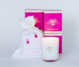 A round, tall white candle with a pink and gold label. The candle is packaged in a pink and gold box with a white ribbon.