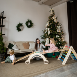 Large wooden Pikler triangle with 2 slides/climbing ladders and balance rocker in rainbow, mint, and pastel colors.