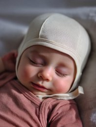 A cozy, natural-colored merino wool baby hat with a bow detail. The hat features a soft, warm design perfect for keeping little ones comfortable in cooler weather.