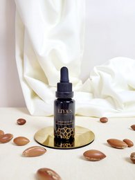 Prickly pear, argan, and organic neroli serum in a glass bottle with a dropper. The serum is dark in color and sits on a white background with some nuts or seeds.