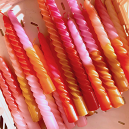 Set of 4 twisted dip-dyed dinner candles in shades of red, pink, and orange. Tall, spiral-shaped candles with a vibrant, ombre color effect.