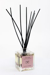 A reed diffuser with a glass bottle and black reed sticks, packaged in a brown box. The product is called "LOVE Story" and is categorized as a room fragrance.