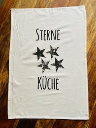 A white kitchen towel with the text "Sterne Kuche" (German for "Star Kitchen") and four black star icons printed on it.