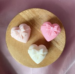 Heart-shaped candles in various pastel colors including pink, yellow, and blue. The candles have a bow-like design on the top, creating a decorative and romantic aesthetic.