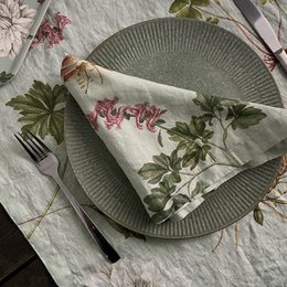 Linen napkin featuring a floral botanical print with leaves, flowers, and a central chrysanthemum-like bloom. The design has a vintage, nature-inspired aesthetic.