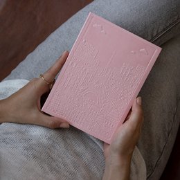 A pink, textured notebook with an embossed city map design. The notebook has a soft, pastel pink cover with a raised, geometric pattern that resembles a city map or architectural layout.