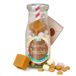 A glass bottle filled with caramel chocolate drinking chocolate mix, including chocolate chunks and marshmallows. The bottle is labeled "Handmade Trinkschokolade" (Handmade Drinking Chocolate).
