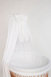 A white textile set for a bassinet, including a canopy with ruffles and a soft, plush bedding. The set is available in cream, white, patina green, and light gray colors.
