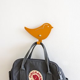 Orange bird-shaped wall hook for hanging kids' clothing and accessories. Made of durable plastic with a sturdy metal hook.