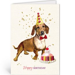 A dachshund dog wearing a party hat and sitting next to a birthday cake with candles. The image has a festive, celebratory feel with confetti in the background.