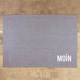 Gray placemat with the word "MOIN" printed on it. The placemat is made of a durable material and is suitable for use in a kitchen or dining area.