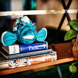 Soft, plush, blue-colored stuffed animal with large eyes and fins, sitting on a stack of books with a Paris theme.