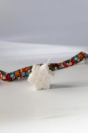A round, tall white soy wax candle with a colorful patterned woven wick holder.