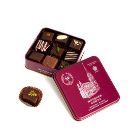  A rectangular tin box containing assorted gingerbread pralines. The box has a red and gold design, and the pralines inside appear to be dark chocolate-coated with various fillings.
