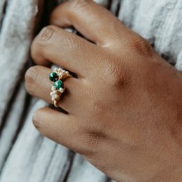Elegant gold-toned statement ring with emerald-colored stones, featuring a unique floral design.