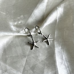 Silver hoop earrings with a starfish charm. The earrings feature a simple, elegant design with a silver starfish pendant hanging from the hoop.