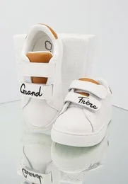 White leather kids' shoes with 'Grand' and 'Tango' text and colorful accents. Suitable for casual wear.