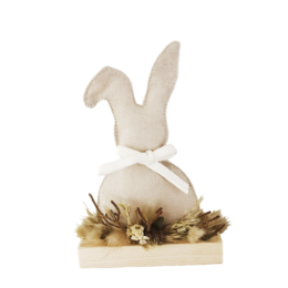 A decorative Easter ornament featuring a white rabbit-shaped figure on a wooden base with dried flowers and foliage.
